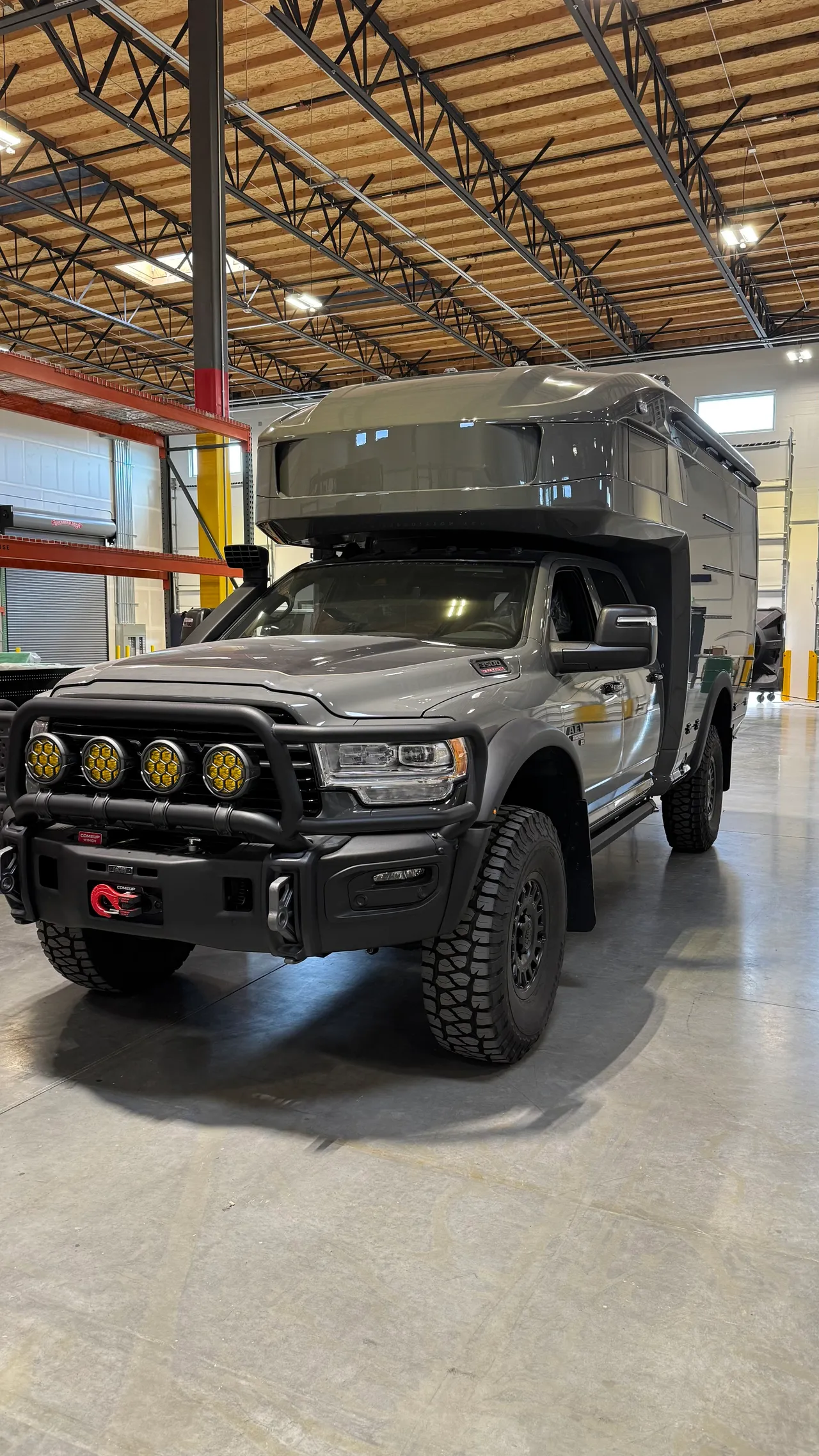 A gray composite camper on a crew-cab pickup parked inside a large shop.