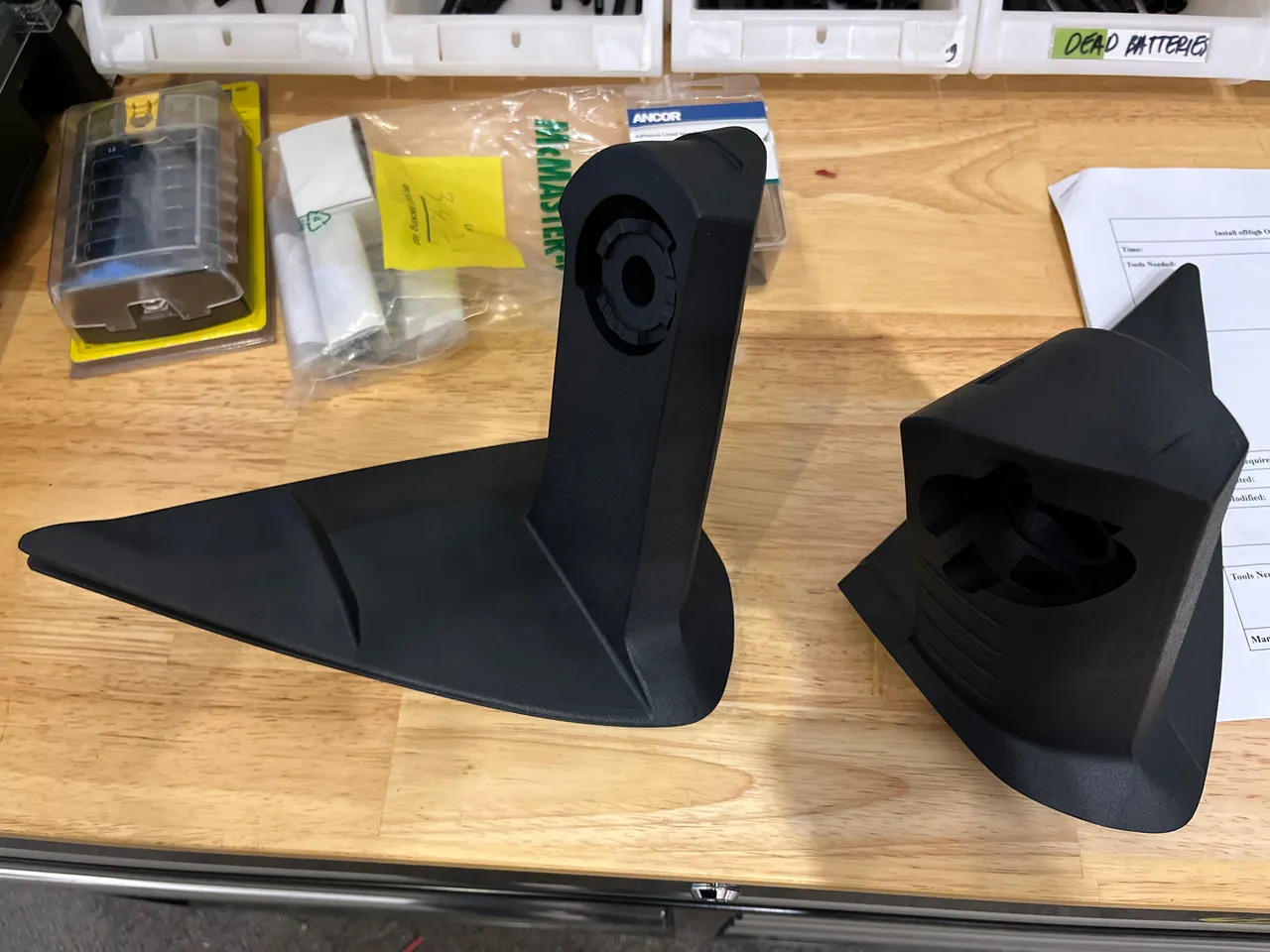 Two printed black mirror extension parts on a wooden workbench next to bagged hardware.