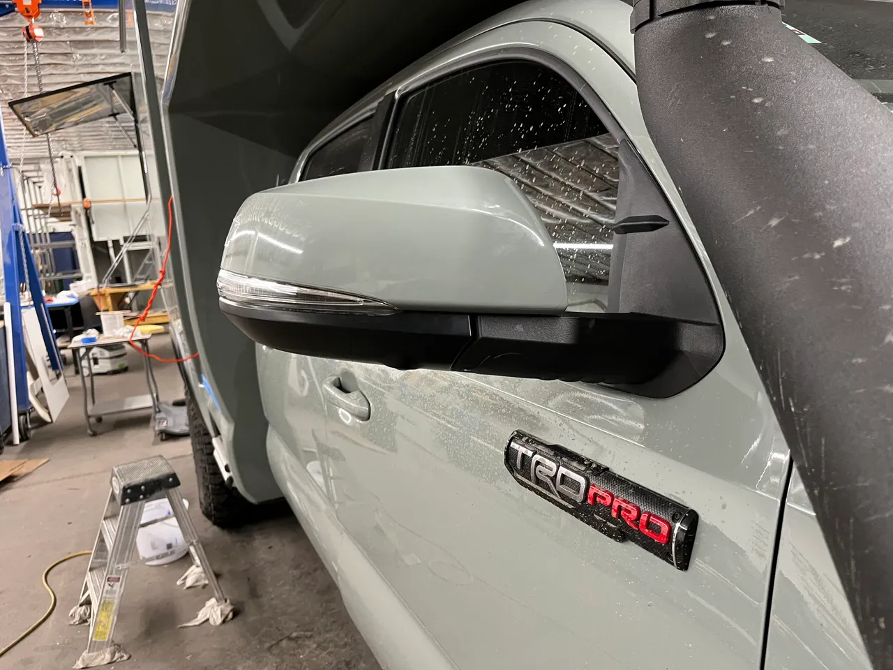 The extended mirror installed on the pickup's door, the mirror head pushed outward on a black extension arm beside the camper.