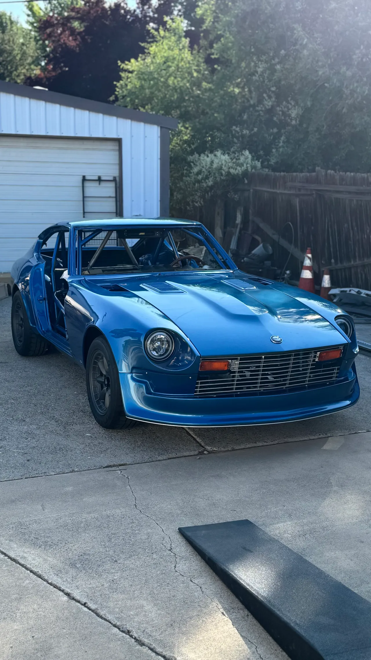 Donna, a metallic blue Datsun Z with a roll cage visible through the windshield, hood vents and a wide front air dam, parked on a driveway.