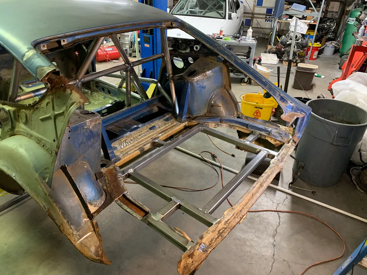 The rear of the body with the corroded floor cut away and a new welded square-tube frame in its place, the roll cage behind it.