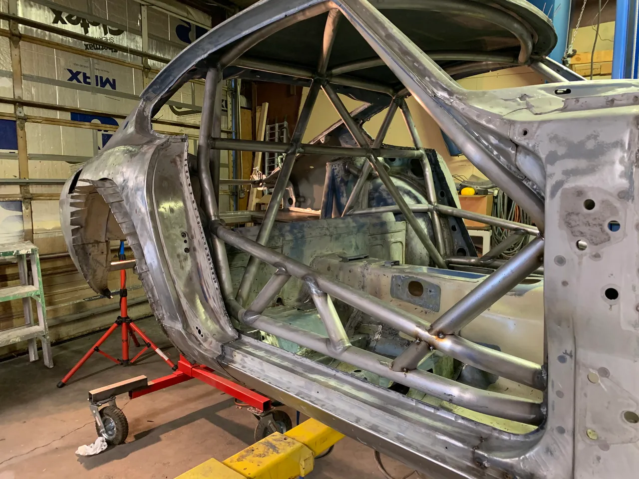 Bare-metal Z body on a rotisserie in the garage, with the welded tube roll cage visible through the door opening.