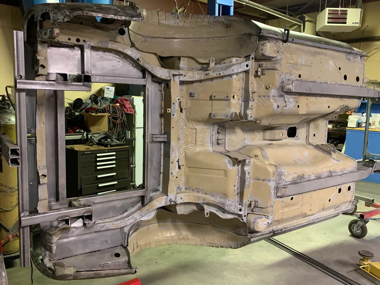 Underside of the stripped body rolled on its side, showing welded frame rails and reinforcement tubes along the floor.