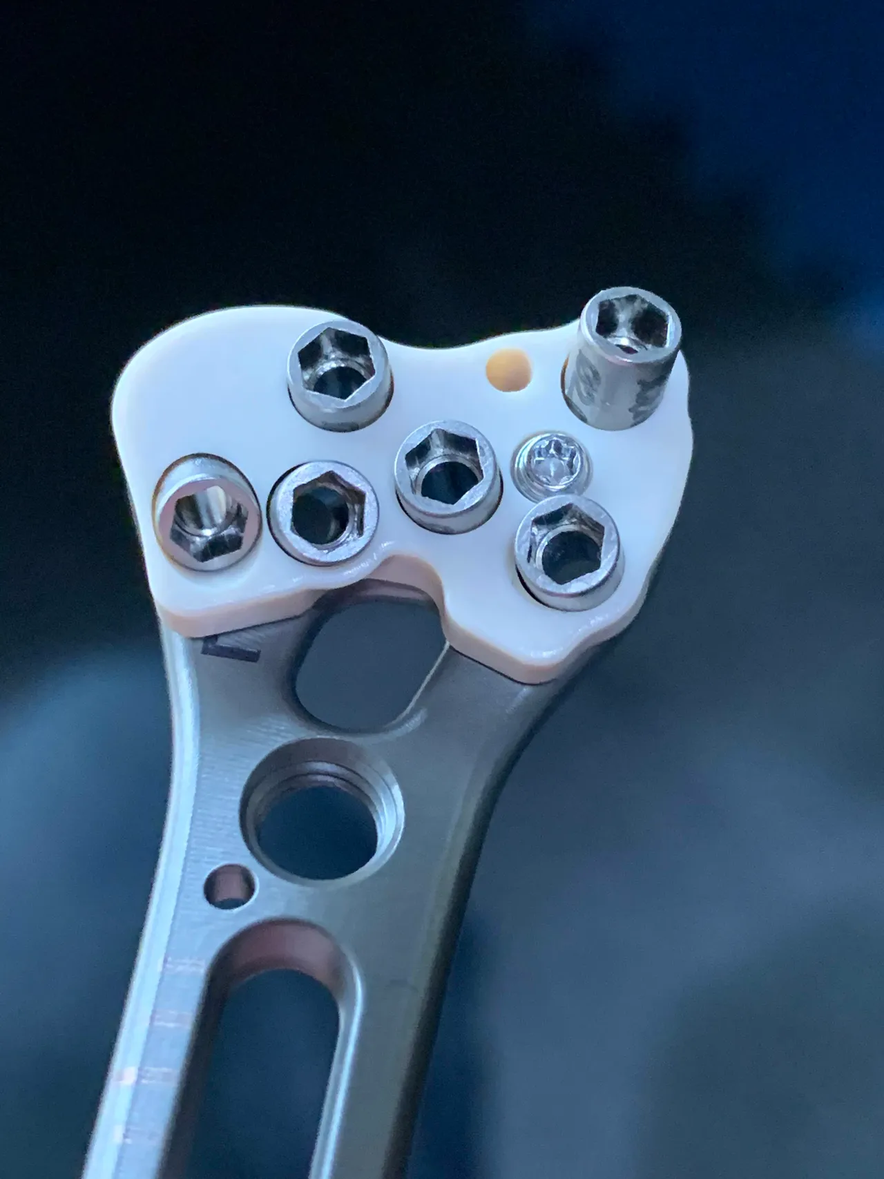 Close-up of a white drill guide block seated on the head of a plate, with metal drill sleeves set into each screw hole.