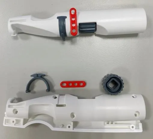 Molded white handle halves laid out with a gray clip, a red perforated strip and a gray knurled thumb-wheel, showing the inside of the handle.