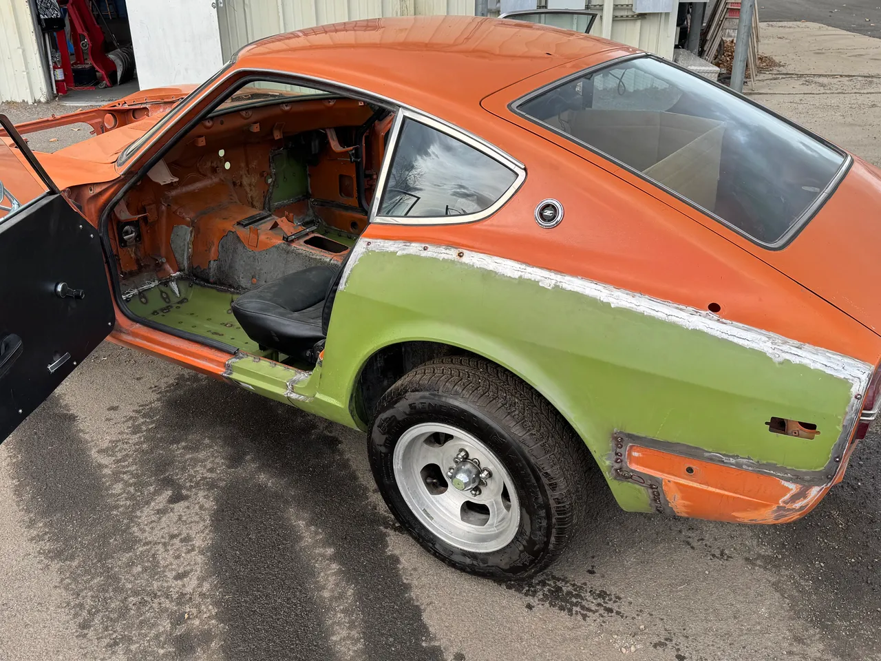 SherryZ, an orange Datsun 240Z with its door open and the interior stripped, the rear quarter panel patched in green primer with fresh welds along the seams.